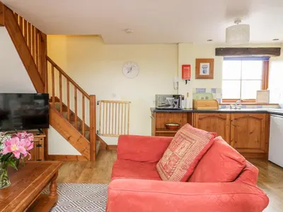 a living room with a red couch and a kitchen at Lavender Cottage in Penrith