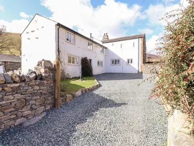 a white house with a stone wall and a driveway at One Town End in Penrith