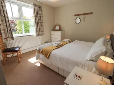 a bedroom with a bed and a chair and a window at Limhus Cottage in Keswick