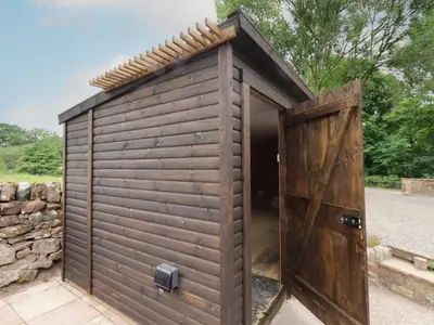 a wooden shed with a door and a stone wall at Lucys cottage in Canonbie