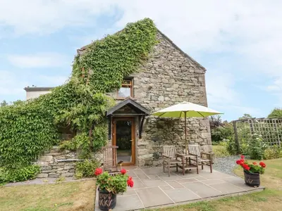 a stone cottage with a table and an umbrella at Poppy Cottage in Penrith