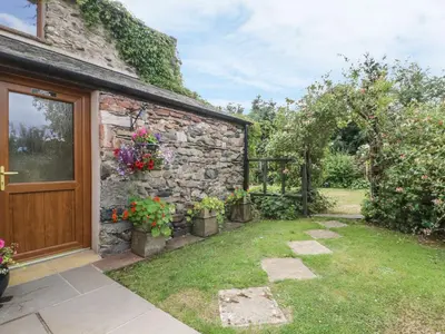 a stone house with a door and some flowers at Poppy Cottage in Penrith