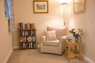 a room with a chair and a book shelf with books at Honeybee Cottage in Penrith