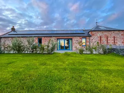 a brick house with a lawn in front of it at The Stables - Luxury Cottage in Dumfries