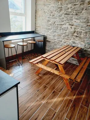a wooden picnic table in a room with a stone wall at Voyage Hostel - Rooms with Shared Kitchen in Douglas