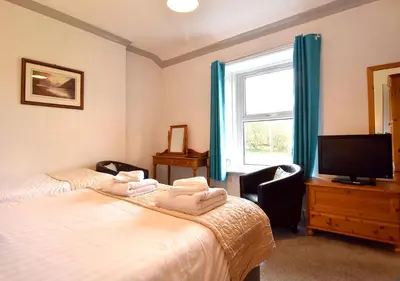 a bedroom with two beds and a tv and a window at Brook House Inn in Eskdale