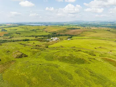 an aerial view of a green field with buildings on a hill at The Kites Rest at Castle Creavie Farm in Kirkcudbright