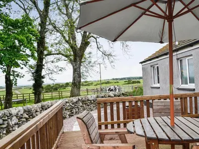 a wooden deck with a table and an umbrella at High Threave Cottage in Newton Stewart