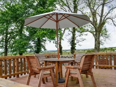 a table and chairs with an umbrella on a deck at High Threave Cottage in Newton Stewart
