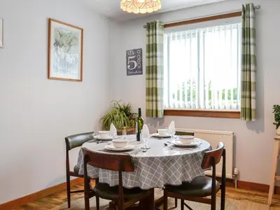 a dining room with a table with chairs and a window at High Threave Cottage in Newton Stewart
