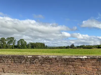 a brick wall in front of a field with a sky at Low Moat in Canonbie