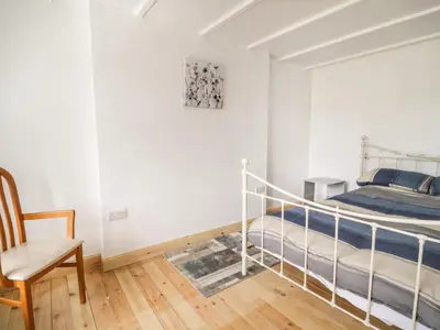 a white bedroom with a bed and a chair at Shaw Cottage in Dumfries