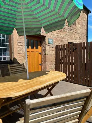 a wooden table with a green and white umbrella at Kitty’s Place, Apartment, Eden Valley, Cumbria in Brampton