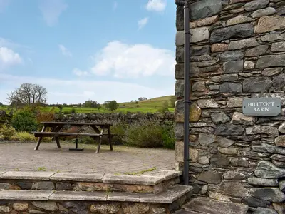 a picnic table next to a stone wall with a sign at Hilltoft Barn in Dockray