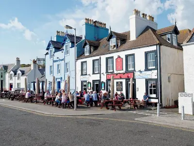 a group of people sitting on benches in front of buildings at Seaviews And Hot Tub At Admirals Anchor in Portpatrick