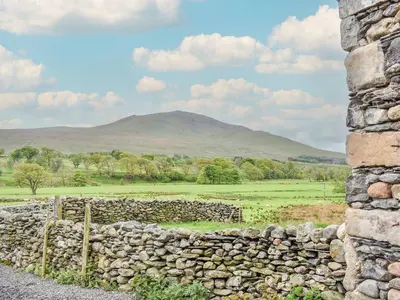 a stone wall with a field and mountains in the background at Doddick Beck - Uk39153 in Threlkeld