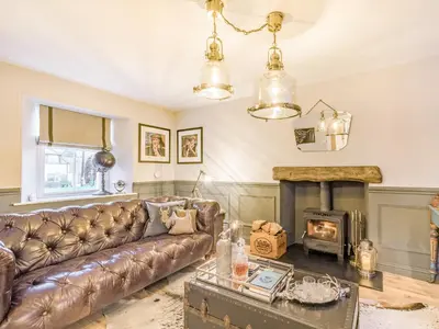 a living room with a leather couch and a fireplace at Keepers Cottage in Durisdeer