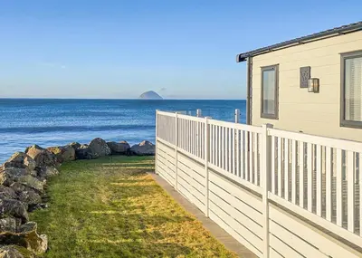 a house with a fence next to the ocean at Bennane Shore Holiday Park in Lendalfoot