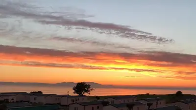 a sunset over a city with houses and the ocean at Arran View Apartment at Heads of Ayr in Ayr