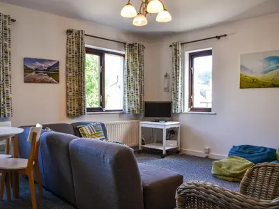 a living room with a couch and a tv and two windows at Buttermere Apartment in Keswick