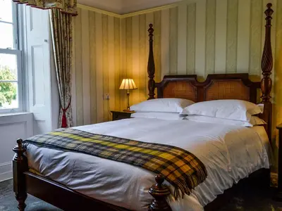 a bedroom with a bed with a plaid blanket on it at Craigvar House in Castle Douglas