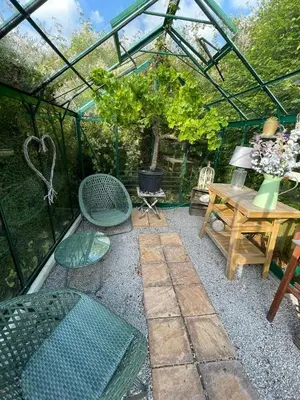 a garden with a greenhouse and a table and chairs at Shelley Cottage in Keswick