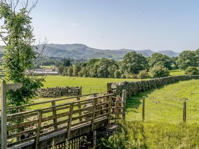 a wooden fence in a field with trees and hills at 1, The Barns in Threlkeld