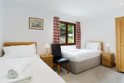 a bedroom with two beds and a chair and a window at Keiras Cottage in Ambleside