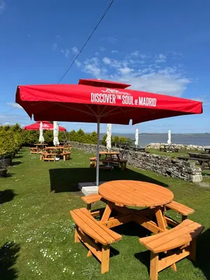 a picnic table with a red umbrella and benches at The Auld Byre - by the Beach in Dumfries
