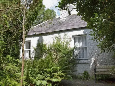 a white brick house with a bench in front of it at Gardener's Cottage in Palnure