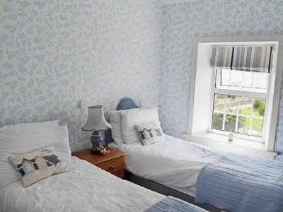 two beds in a bedroom with blue wallpaper at Coastguard's Cottage in Carsethorn