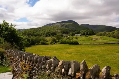 a stone fence in a field with mountains in the background at Lowfield House in Ambleside