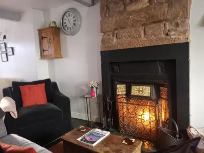 a living room with a fireplace and a chair at Mill Cottage modern cosy Lake District home with open fire near Scafell in Gosforth