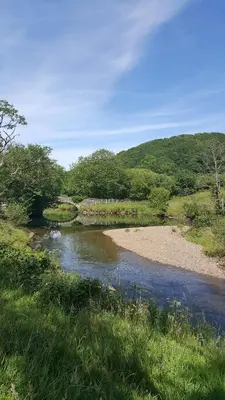 a river in the middle of a field with a bridge at Mill Cottage modern cosy Lake District home with open fire near Scafell in Gosforth
