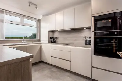 a kitchen with white cabinets and a window at West Sands - Donnini Apartments in Ayr