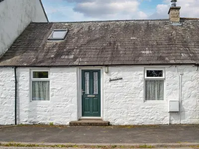 a white building with a green door and windows at Kerrim Cottage in Ringford
