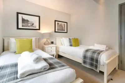 two beds in a room with white walls and yellow pillows at Jontys Cottage in Ambleside