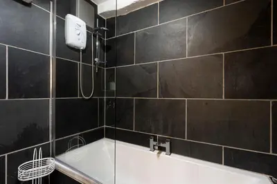 a bath tub in a bathroom with black tiles at Jontys Cottage in Ambleside