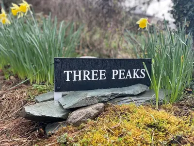 a three peaks sign sitting on rocks in a garden at Three Peaks in Braithwaite
