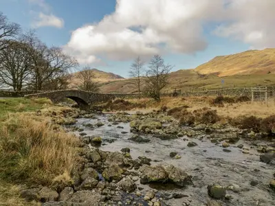 a stream with a bridge and mountains in the background at Newfield Apartment 1 in Broughton in Furness