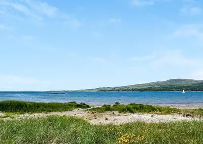 a beach with a body of water with a boat in it at Sandgreen Caravan Park in Girthon