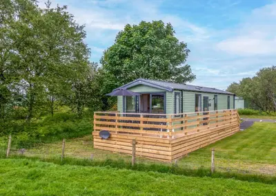 a tiny house with a large deck in a field at Sandgreen Caravan Park in Girthon