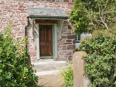 a brick house with a wooden door and stairs at Caldhu Cottage in Holmrook