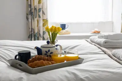 a tray of food and orange juice on a bed at Finest Retreats - The Cottage at Greystoke in Greystoke