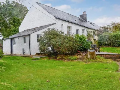 a white house with a tree stump in the yard at Howbeck Cottage in Hesket Newmarket