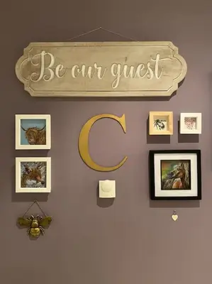 a wall with pictures and a sign that says be our guest at Courtyard Cottage in Lockerbie