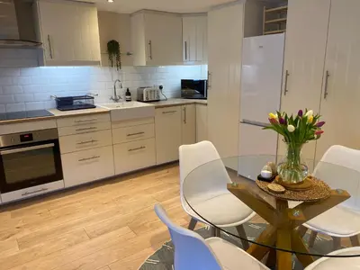 a kitchen with a glass table and white chairs at The Workshop, Bridge House in Laxey