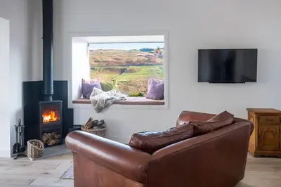 a living room with a leather couch and a fireplace at Croft Cottage in Gatehouse of Fleet