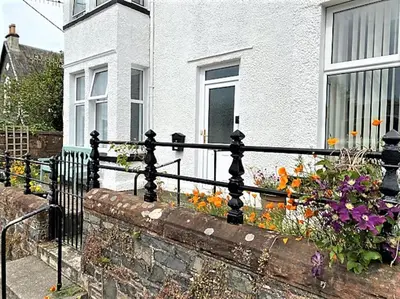 a fence in front of a white house with flowers at St John's Flat Spacious Accomodation in Dalry