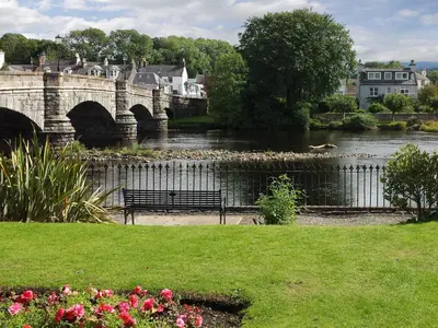 a bench next to a river with a bridge at Park Crescent - Cottage in Creetown